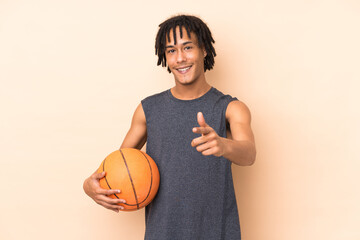 Young african american man isolated on beige background playing basketball and pointing to the front