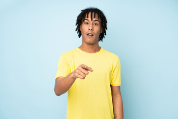 Young african american man isolated on blue background surprised and pointing front