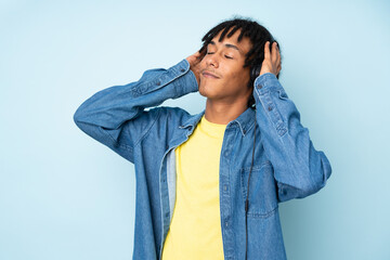 Young african american man isolated on blue background listening music and dancing