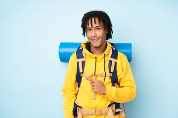 Young mountaineer african american man with a big backpack isolated on a blue background pointing...