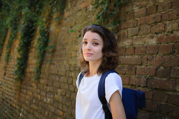 Female portrait of beautiful student, pretty girl with short hair in white t-shirt spending time outdoors near old stone wall during sunny spring or summer day