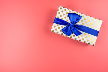 A gift wrapped in white paper with gold circles wrapped in a blue ribbon tied in a bow, isolated on...