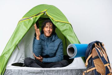 Young african american man inside a camping green tent extending hands to the side for inviting to come