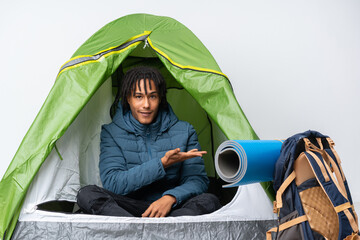 Young african american man inside a camping green tent presenting an idea while looking smiling towards