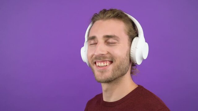 close-up portrait of a young smiling man in big white headphones.Man .young man dancing head. Isolated on purple background.