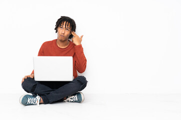 Young african american man sitting on the floor and working with his laptop with problems making suicide gesture