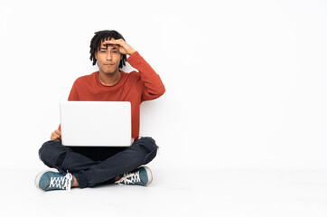 Young african american man sitting on the floor and working with his laptop looking far away with hand to look something