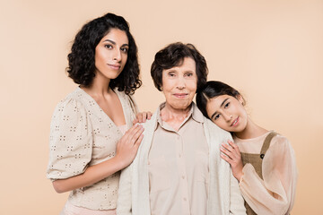 Hispanic kid and woman hugging grandmother and looking at camera isolated on beige, three generations of women