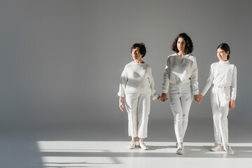 Three generations of hispanic women smiling while walking on grey background