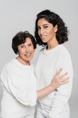 Elderly hispanic woman hugging cheerful daughter isolated on grey, two generations of women