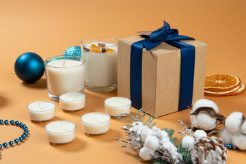decorations for the new year, christmas. natural candles made of wax, gift, box with blue ribbon, orange background, pastel soft colors.