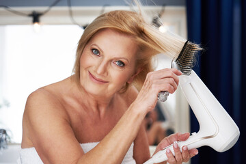 Senior woman drying hair in the bathroom