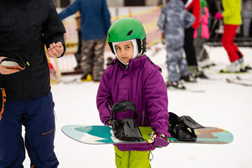 Fototapeta premium Snowboard Winter Sport. little girl learning to snowboard, wearing warm winter clothes. Winter background.