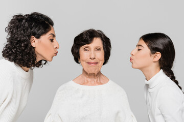 Hispanic woman and girl kissing smiling granny isolated on grey, three generations of women