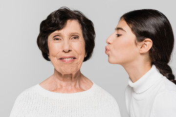 Hispanic kid kissing smiling granny isolated on grey, two generations of women