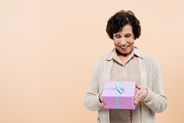 Elderly hispanic woman holding present and smiling isolated on beige