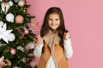 Obraz na płótnie Canvas happy little child girl holding lollipop candy cane on the pink background of christmas tree. copy space