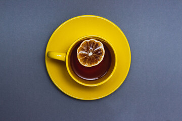 Hot black tea with lemon slice top view on gray background. Yellow cup on gray. Colors of the year...