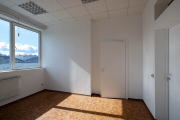 Modern interior of empty office room. White walls and door. Huge window. Sunny day.