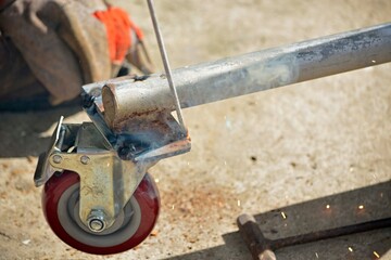Worker with a welding machine fixing a caster wheels, sparks flying around