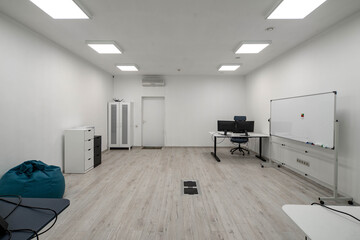 Modern light interior of spacious office room. Computer on table. Marker board. Cozy beanbag chair.