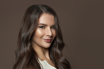 Perfect young woman face with healthy clear skin and long curly hair on brown background