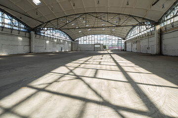 Huge empty industrial warehouse. White interior. Unique architecture. Hemispherical reinforced concrete load bearing roof with windows. Shadow of construction on floor.