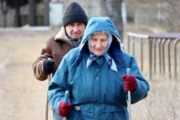 Nordic walking, elderly couple walk with canes in a park. Sports exercises for healthy spine and...