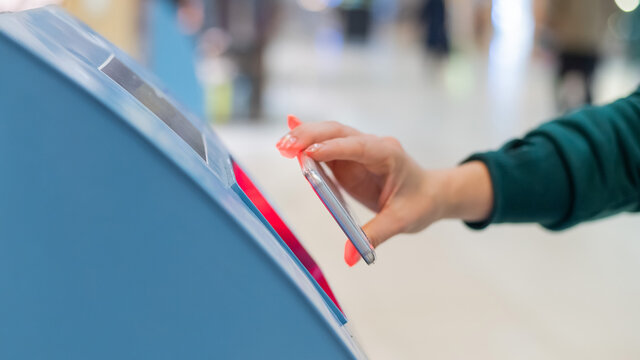 A faceless woman scans the qr code from her smartphone. A girl uses a self-service machine at the airport to check in for a flight and print tickets