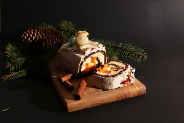 Beautiful Christmas cake, decorated with fir branches with a pine cone on a wooden board. The background is black.