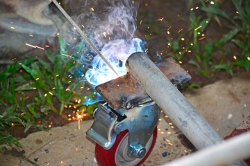 Worker with a welding machine fixing a caster wheels, sparks flying around