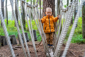Young Child Playing on Rope Obstacle Track in Woods - Caucasian Boy Wearing Orange Raincoat