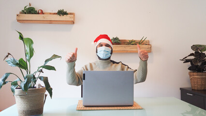 Man with Santa hat and medical mask making a video call with laptop from an office
