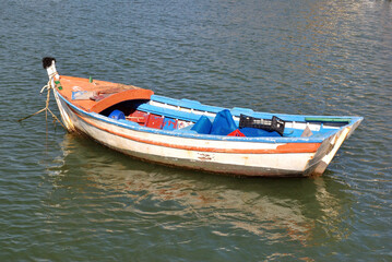 Naklejka na ściany i meble Colourful Empty Rowing Boat Anchored in Rippled Waters 