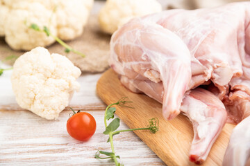Whole raw rabbit with cauliflower, tomatoes and spices on a white wooden background. Side view, selective focus.