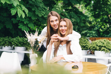 Naklejka premium Joyful adult daughter hugs her mother and holds flowers for her. Birthday surprise for mom
