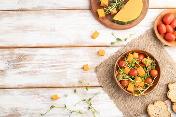 Vegetarian vegetable salad of tomatoes, pumpkin, microgreen pea sprouts on white wooden background. Top view, copy space.