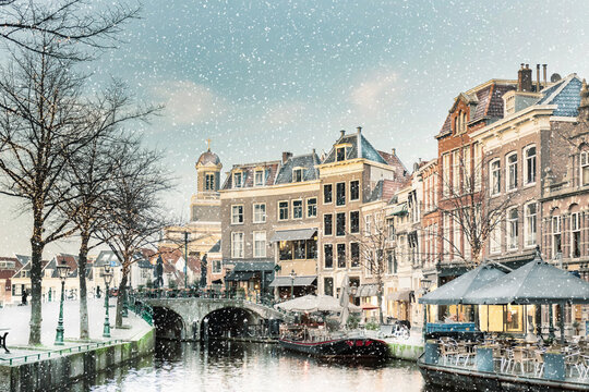Winter view with snowfall of the Dutch Nieuwe Rijn canal with bridge and historic buildings in the city center of Leiden