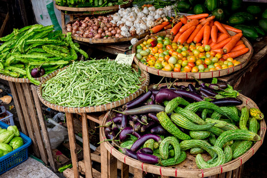 A selection of bitter gourds, eggplants, green beans, tomatoes, winged beans, carrots, onions and garlic at a Philippine market. Several flies swarm and land on the vegetables, raising health issues