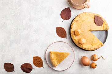 Autumn onion pie decorated with leaves and cup of coffee on gray concrete background. Top view, copy space.