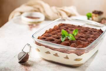 Traditional Italian dessert tiramisu in a glass backing form on light background