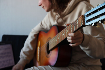 A girl is playing the guitar and watching notes on a laptop. 