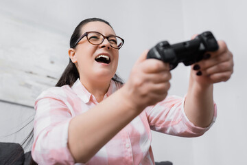 KYIV, UKRAINE - DECEMBER 07, 2020: Low angle view of excited plus size hispanic woman playing with joystick on blurred foreground