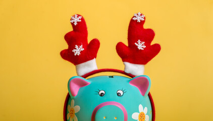 Piggy bank isolated on yellow. Blue piggybank on Christmas. Bank with deer antlers. Saving for new year