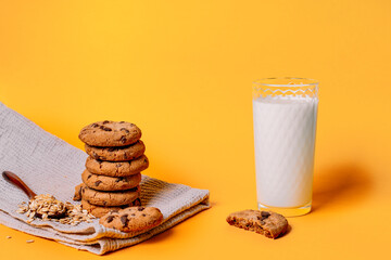Oatmeal chocolate chip cookies and a glass of milk on a kitchen towel on a yellow background with space for text