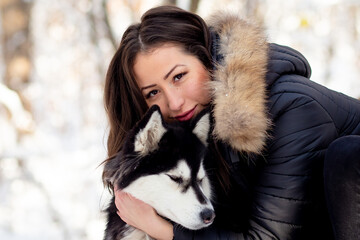 Beautiful young woman hugging female husky dog in cold winter snowy day