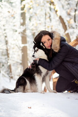 Beautiful young woman hugging female husky dog in cold winter snowy day