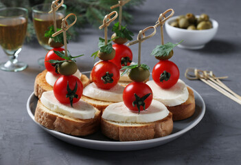 Canapes of mozzarella, cherry tomatoes, green olives, parsley on croutons of white bread on dark gray background. Festive New Year snack. Closeup