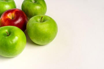 Green apples and one red one are laid out on a white table