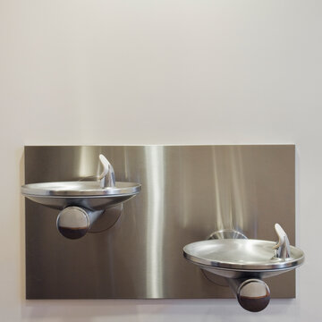 Two metal drinking fountains mounted on wall at different heights.